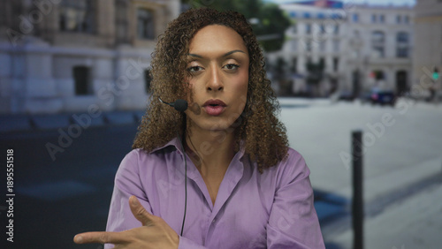 Obraz na plátne Transgender woman wearing headset microphone gestures hand while speaking on busy street in daylight; confidence