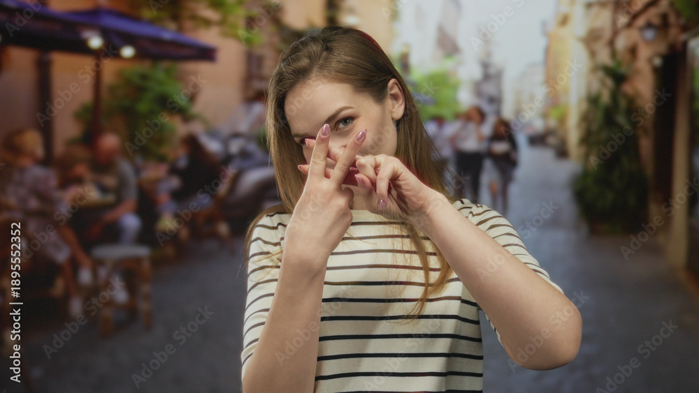 Fototapeta premium Woman crossing index fingers in front of her on a busy street terrace by cafe tables under umbrellas with a playful smile; rejection.