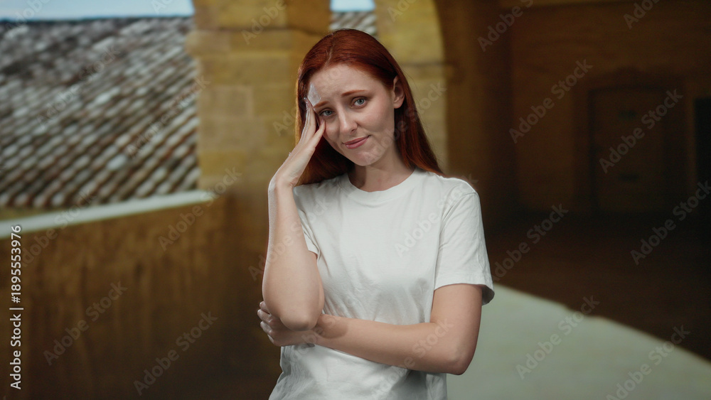 Fototapeta premium Woman standing in outdoor university courtyard with hand on head, appearing thoughtful and reflective, showcasing a serene and picturesque academic environment.