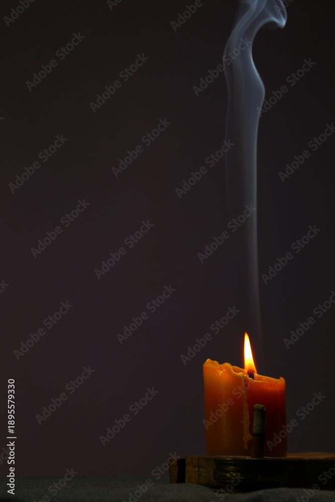 Naklejka premium Blue smooth texture smoke from incense aroma stick in motion rising above in holiday celebration and burning wax candle fire on copy space dark background. Yoga calm meditation, relaxation concept 