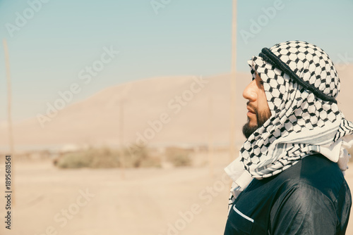 Arab man wearing keffiyeh and looking into distance in desert