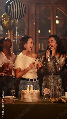 Joyful multiracial friends celebrating a woman's birthday party, making a wish, and blowing out candles on a cake