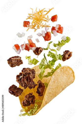 deconstructed beef taco with flying ingredients: seasoned meat, shredded lettuce, diced tomatoes, onions, and cheese over a corn tortilla, isolated.