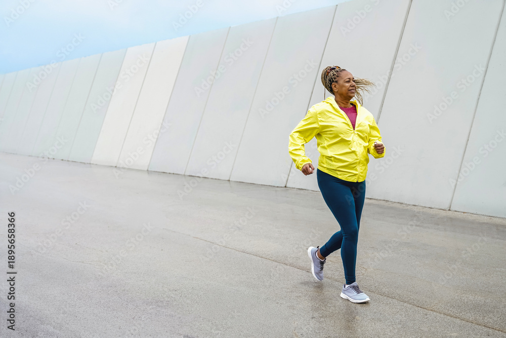 Obraz premium Active senior sport Afro Latina woman running outdoors in cool rainy weather – fitness, wellness and healthy lifestyle concept