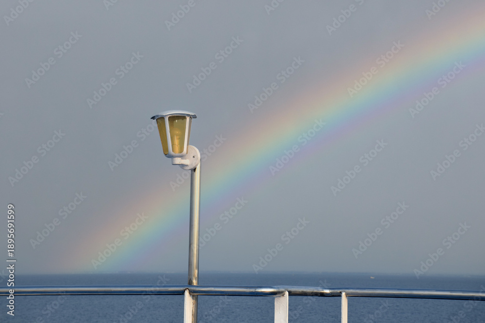 Fototapeta premium A ship's lights against a backdrop of a rainbow before sunset at sea