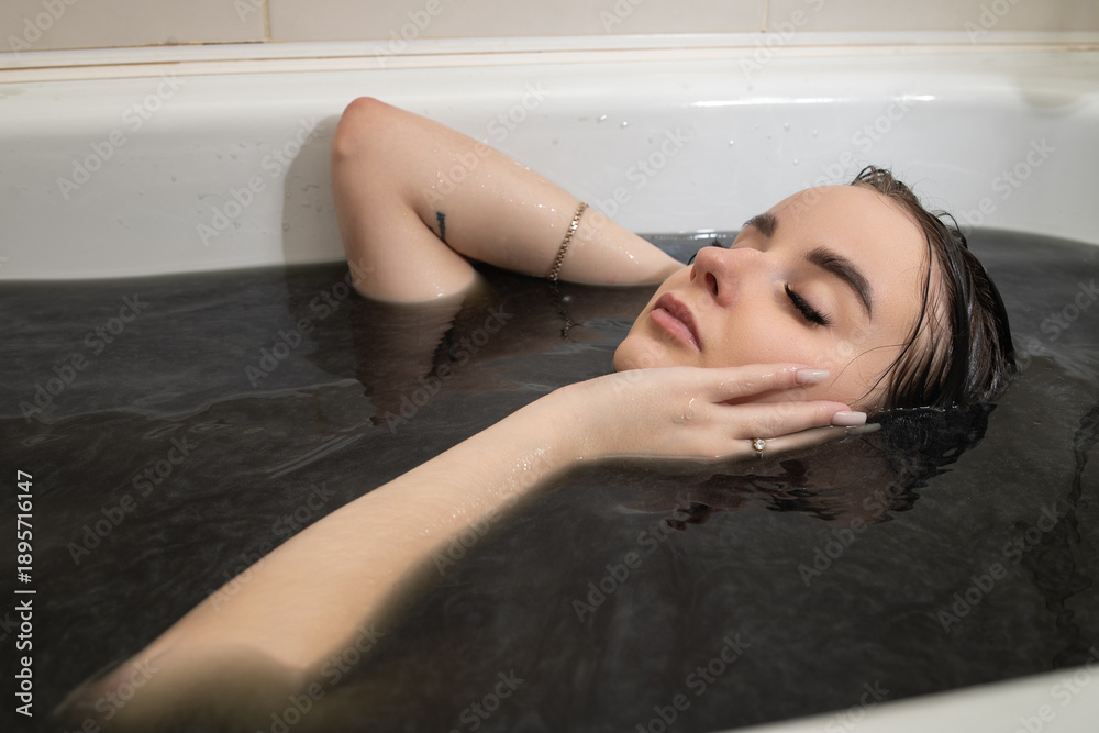 Obraz premium Female figure with long dark hair partially submerged in dark water, facial features visible above the surface, creating a serene and reflective atmosphere