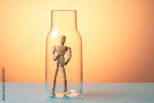Wooden mannequin inside glass jar on orange background, isolation and inner immigration concept