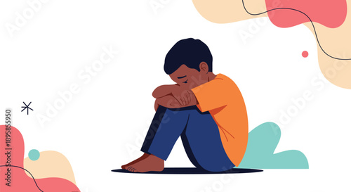 Sad and lonely young boy sits huddled on the floor with his head down expressing feelings of depression and solitude.