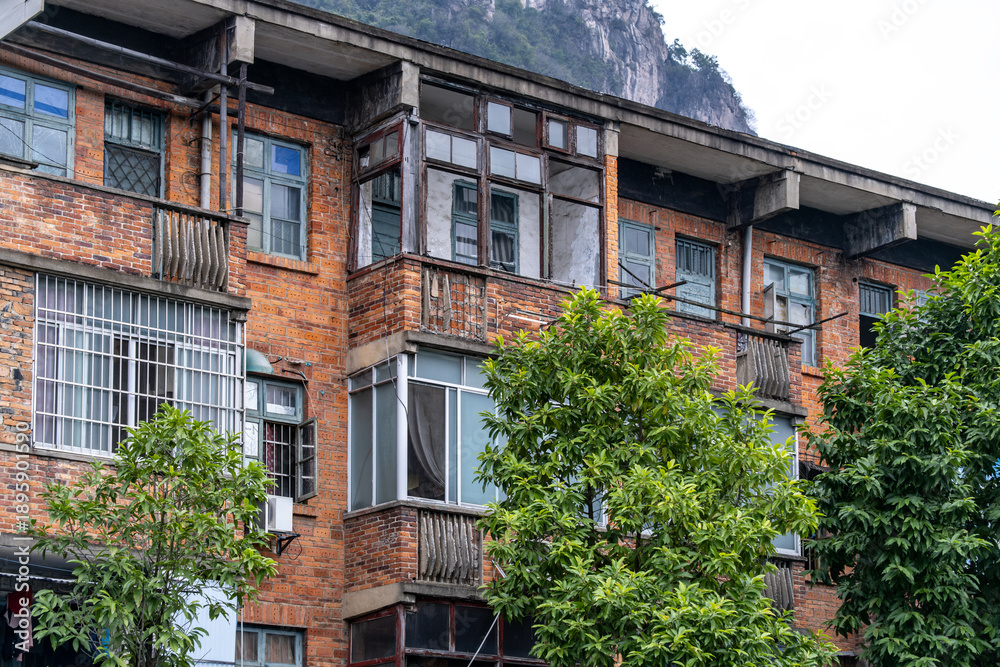 Fototapeta premium An aging brick apartment building with balconies and weathered facades in an older residential neighborhood in China. Urban housing, past-era construction, and poor living conditions