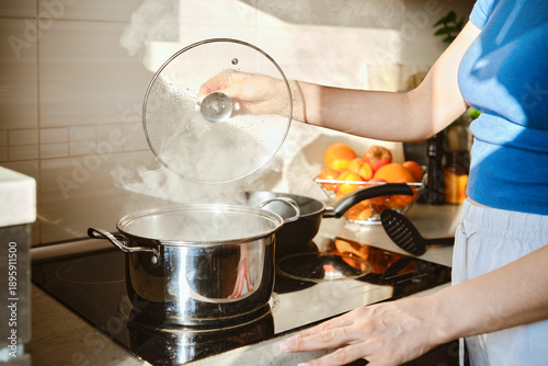 Fotografie Unrecognizable woman lifts the lid of a pot of boiling water