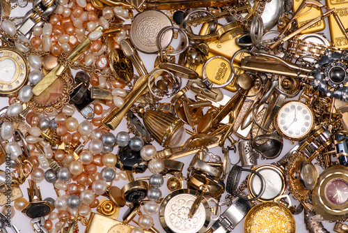 Antique jewelry lies in clutter on a gold background. The jewelry appears second hand. Gold metal defines the antique jewelry background. This background suggests pawnshop value.