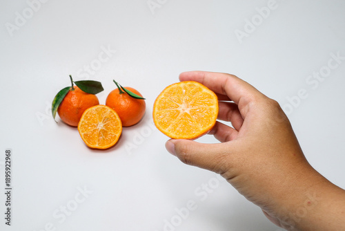 Hand holding fresh orange fruit with slices on isolated white background.
