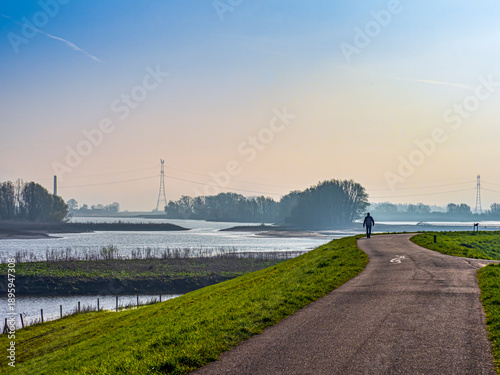 Foto Person walking along Waalbandijk levee by Waal river