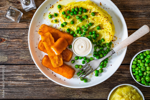 Fried fish fingers with mashed potatoes and green peas on wooden table. Top view