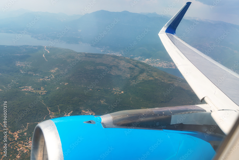 Fototapeta premium High angle view from an airplane window showing the wing and engine over a mountain landscape.