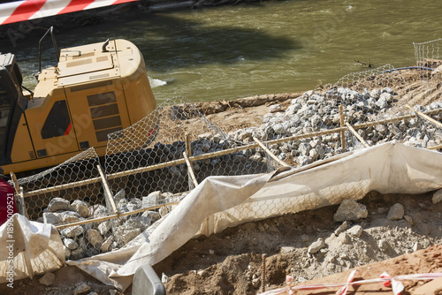 Heavy excavator at construction site for riverbank erosion control. Engineering earthwork with heavy machinery using stone and geotextile for foundation protection