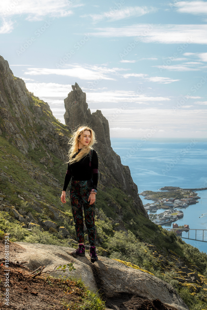 Obraz premium White blonde woman standing on a hike in Lofoten with city in the background