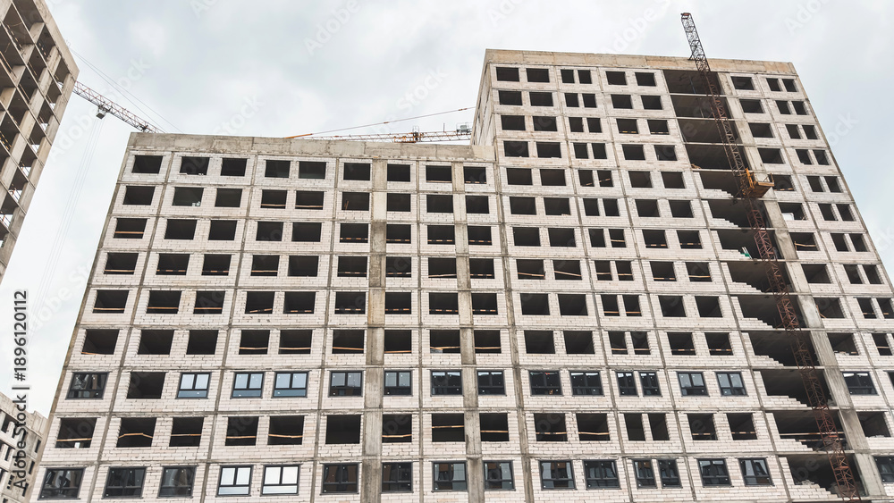 Fototapeta premium Unfinished high-rise apartment building under construction with visible concrete structure and cranes above, symbolizing architecture, engineering, and urban development concepts