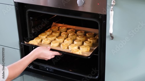 woman gaves homemade cinnamon rolls in tray into oven , green kitchen, real life