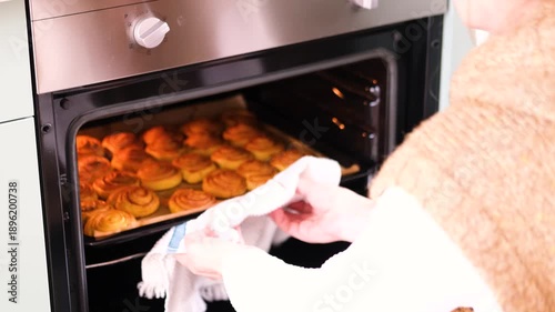 woman takes homemade cinnamon rolls freshly baked from oven