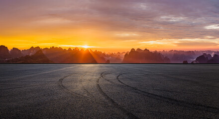 Leinwandbilder Pantone 2025 Mocha Mousse An empty asphalt race track with tire tracks and a beautiful karst mountain landscape under a dramatic sunset sky in Guilin, China.  © ABCDstock