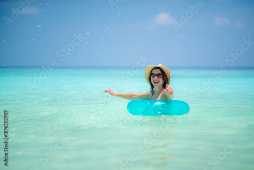 Photography woman floats in turquoise water on sunny day, wearing straw hat and sunglasses,