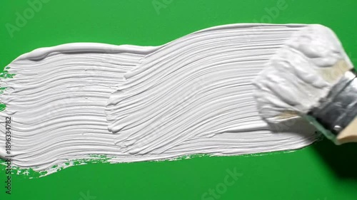 Applying white paint with brush on green background art and creativity