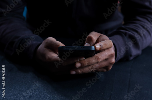 Foto Phone scammers, unrecognizable man holding a smartphone, anonymous cyber criminal performing phishing attack, identity theft via mobile phone, threat to privacy and digital security