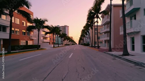 A street with palm trees and a sunset in the background. The street is empty and the buildings are tall
