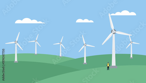 A person standing beside the tallest wind turbine on a green hill under a clear blue sky, watching the wind spin.