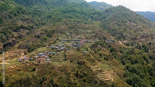 Cinematic aerial view of a peaceful mountain village near Pokhara Nepal surrounded by lush green hills