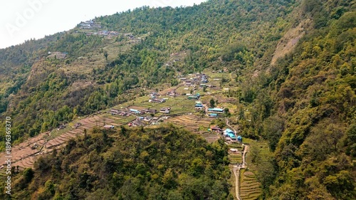 Cinematic aerial view of a peaceful mountain village near Pokhara Nepal surrounded by lush green hills