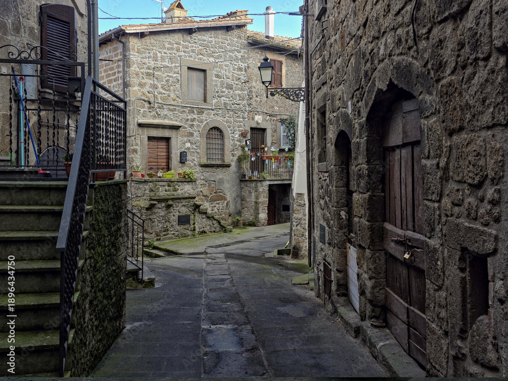 Fototapeta premium A narrow alleyway in the ancient town of Vitorchiano, Italy, defined by unique external stone staircases and grey volcanic rock buildings
