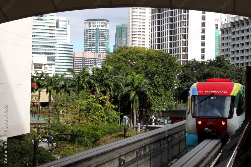 Obraz premium Kuala Lumpur cityscape with modern skyscrapers, tropical greenery and KL Monorail train, showcasing urban transport in a vibrant Asian metropolis.