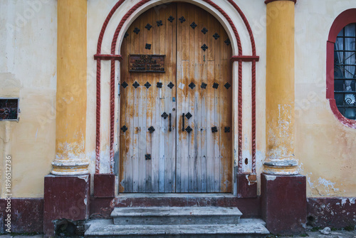 Historic wooden church door with ornate arch and colorful colonial facade in San Cristóbal de las Casas, Mexico.