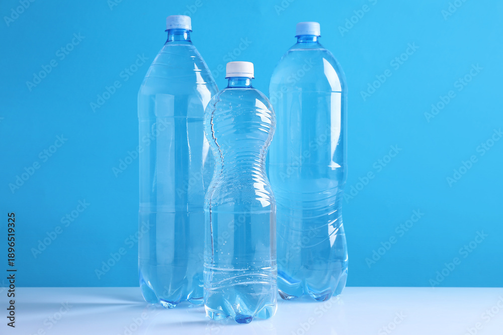 Fototapeta premium Bottles of fresh water on white table against light blue background