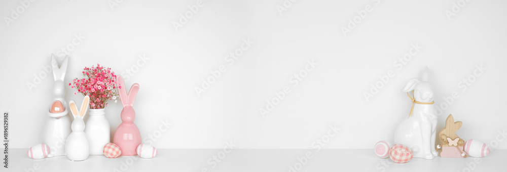 Fototapeta premium Easter decor on a white shelf. Easter bunnies, flowers, eggs against a white wall banner background. Copy space.