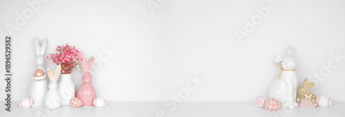 Easter decor on a white shelf. Easter bunnies, flowers, eggs against a white wall banner background. Copy space.