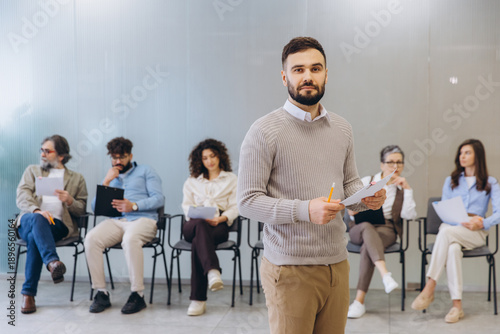 Photos Hr manager holding paper in front of diverse job candidates waiting for intervie