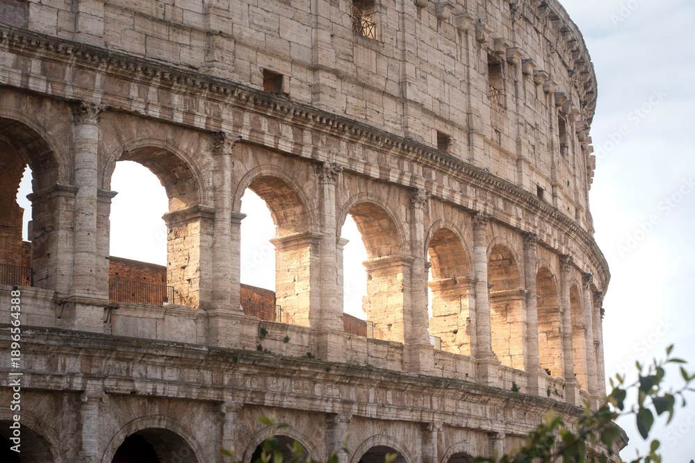Fototapeta premium An intimate, textured close-up of the Colosseum's iconic walls in Rome. Deep grooves, pockmarks, and layered stone blocks of the ancient amphitheater, telling a story of millennia under Italian sun.
