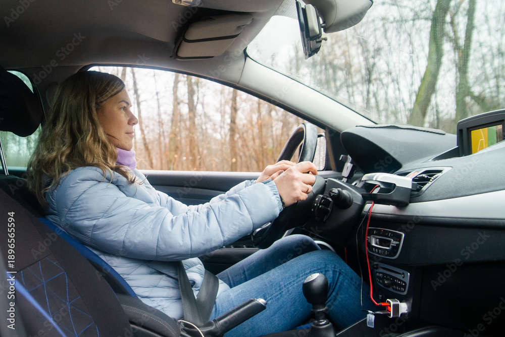 Naklejka premium Young Woman Driving a Car Through a Forest Road in Winter