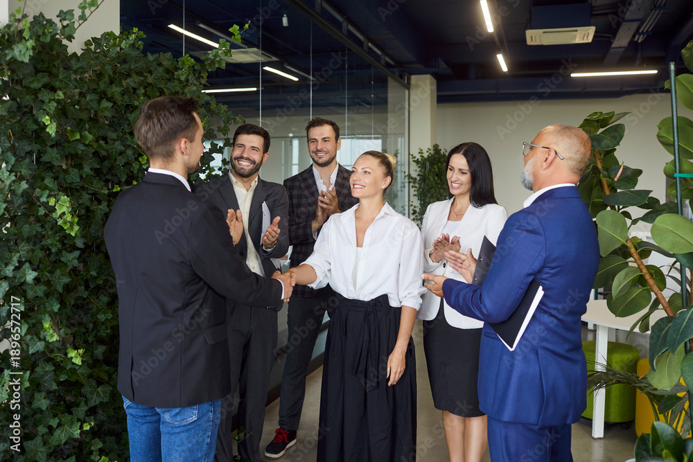 Fototapeta premium Female business leader and man shake hands in applause of colleagues team standing in green office. Happy people applauding handshake to welcome new employee, congratulate on achievement