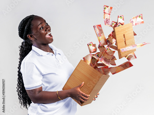 Foto A joyful woman holds a wooden savings box as Ghanaian 200 Cedi notes erupt upward