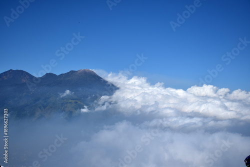 A mountaintop scene with white clouds enveloping it against a backdrop of a clear blue sky