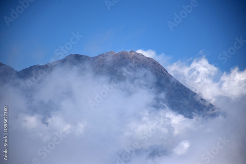 A mountaintop scene with white clouds enveloping it against a backdrop of a clear blue sky