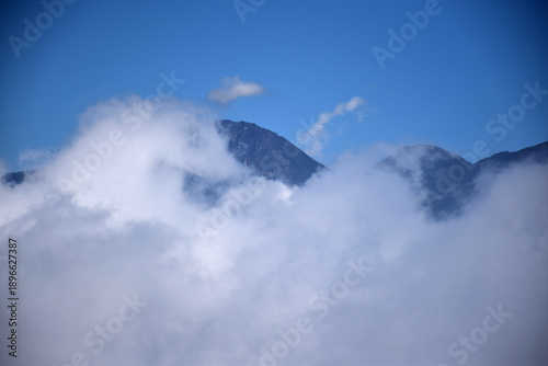 A mountaintop scene with white clouds enveloping it against a backdrop of a clear blue sky