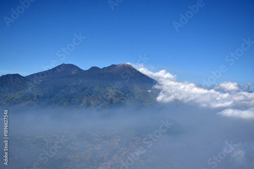 A mountaintop scene with white clouds enveloping it against a backdrop of a clear blue sky