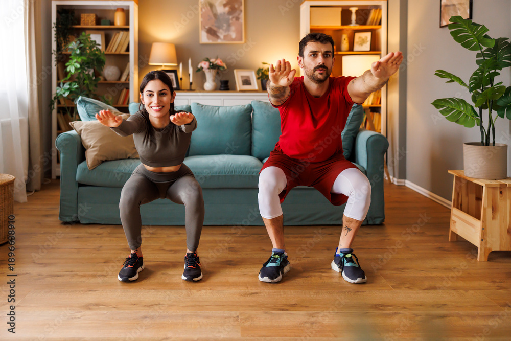 Obraz premium Active couple doing squats exercise while working out at home