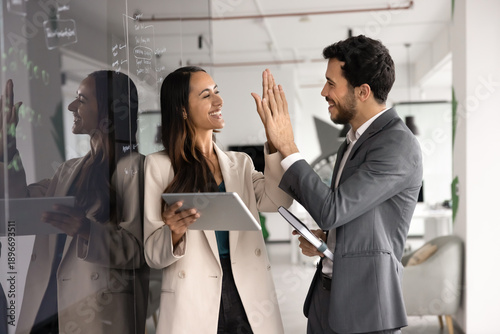 Happy successful teammates exchanging high five stands next to blackboard with written records, finish teamwork, feel satisfied with work done, good results and partnership. Collaboration, efficiency