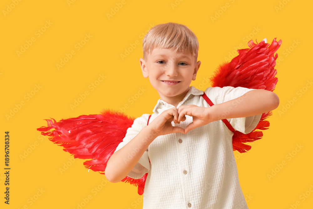 Fototapeta premium Cute little happy boy dressed as cupid showing heart gesture on yellow background. Valentine's Day celebration